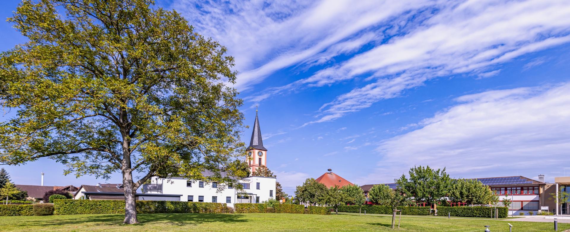 Straße im Winter Der Klosgarten, eine für Festlichkeiten angelegte Rasenfläche, weiße Wolken zeihen am blauen Himmel entlang, hinten ragt die Kirchturmspitze auf