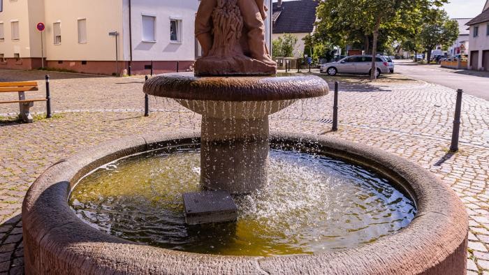 Sonnenplatzbrunnen Sonnenplatz mit dem Fischer- und Bauernbrunnen, einem runden Sandsteinbrunnen, in dessen Mitte je ein Bauer und Fischer abgebildet sind und Rücken an Rücken stehen