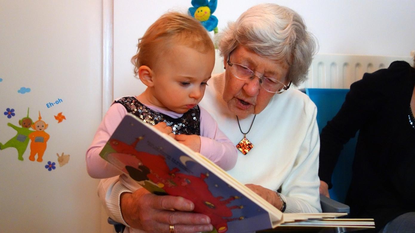 ältere Dame liest kleinem Mädchen, das auf ihrem Schoß sitzt, ein Buch vor
