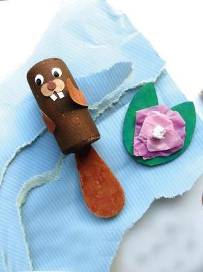 Bockel, der Biber ein selbstgebastelter, brauner Biber mit einem Eisstäbchen als Schwanz und aufgeklebten Augen, Nase, Zähnen und Vorderpfoten liegt auf einem blauen Papier neben einer selbstgebastelten Seerose