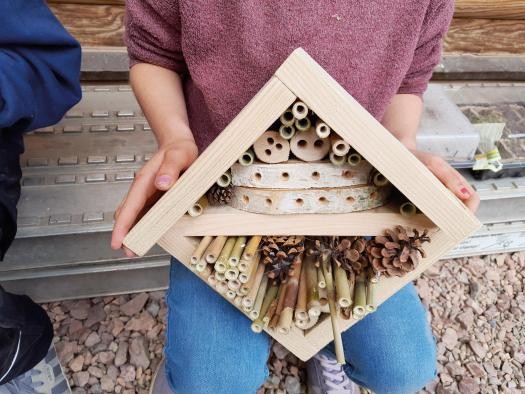 Insektenhotel Eine Person hält ein quadratisches, selbstgebautes Insektenhotel aus hellem Holz