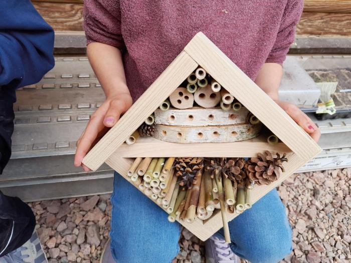 Insektenhotel Eine Person hält ein quadratisches, selbstgebautes Insektenhotel aus hellem Holz