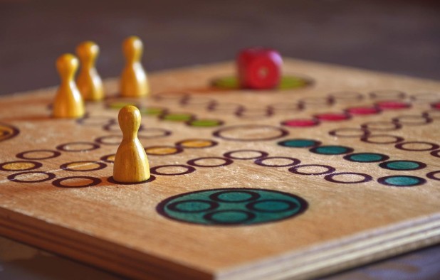 Brettspiel Holzbrettspiel, auf dem gelbe Figuren und ein roter Würfel liegen