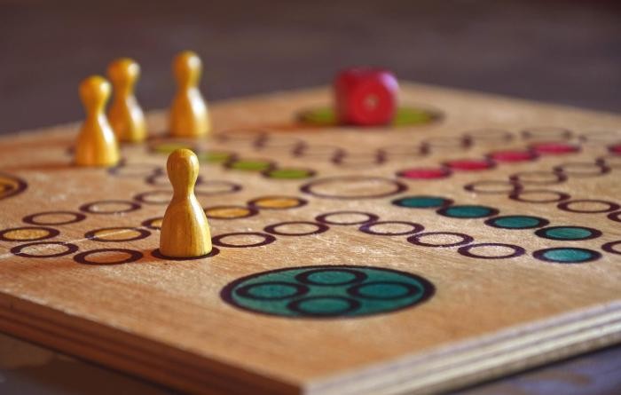 Brettspiel Holzbrettspiel, auf dem gelbe Figuren und ein roter Würfel liegen