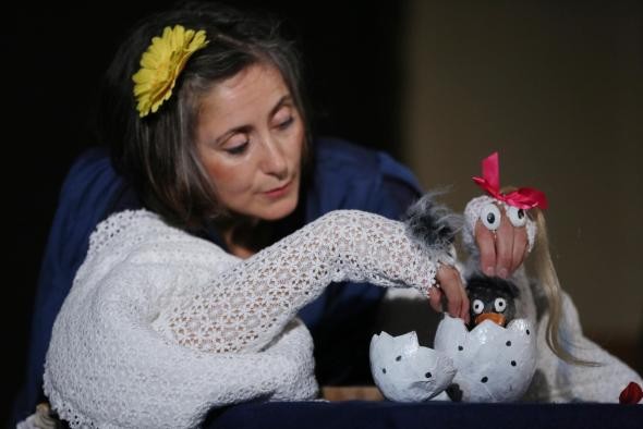 Eine Frau die Handpuppen hält, vor ihr liegt eine Eierschale mit einem kleinen Küken darin Eine Frau die Handpuppen hält, vor ihr liegt eine Eierschale mit einem kleinen Küken darin