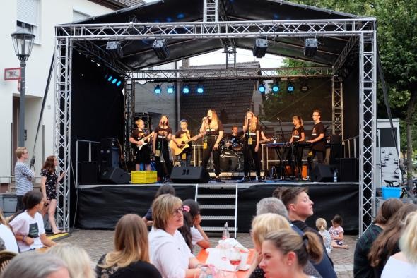 Schülerbandcontest Eine große Schülerband steht auf einer Bühne, davor sieht man Zuschauer, die an Bierbänken sitzen