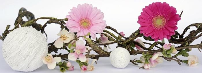 Frühlingserwachen ein Ast mit Kirschblüten ist dekoriert mit weißen Kugeln und rosa und pinken Gerbera