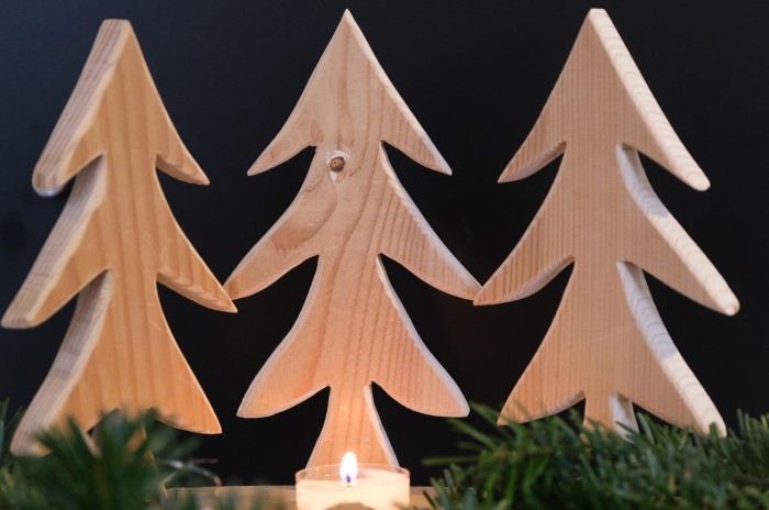 Weihnachtsdeko drei Holztannenbäume, selbst ausgesägt, stehen hinter Tannenzweigen und einem mittig platzierten Teelicht