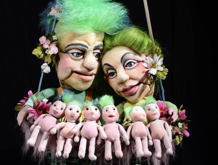 Die Zauberflöte Zwei große Puppen, Mann und Frau, haben vor sich in den Armen sechs kleine Babypuppen