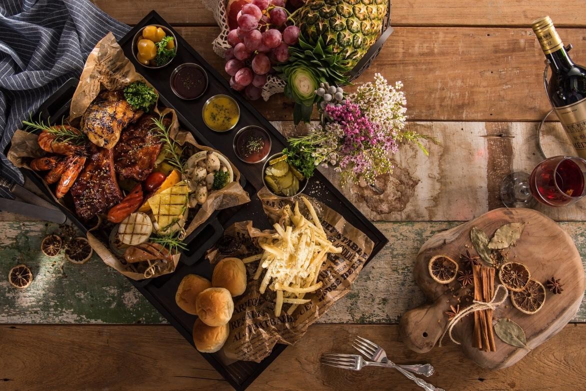 Gastronomie Holztisch mit dicht belegtem Tablett voller Essen, Gewürzen, Wein und Besteck