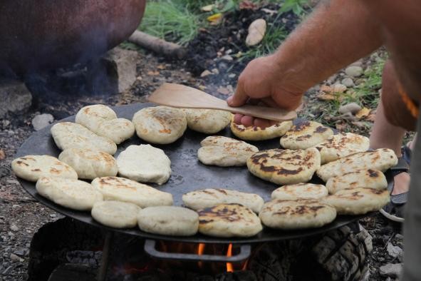 kleine Fladen werden auf einer Pfanne über einem Lagerfeuer gebraten kleine Fladen werden auf einer Pfanne über einem Lagerfeuer gebraten